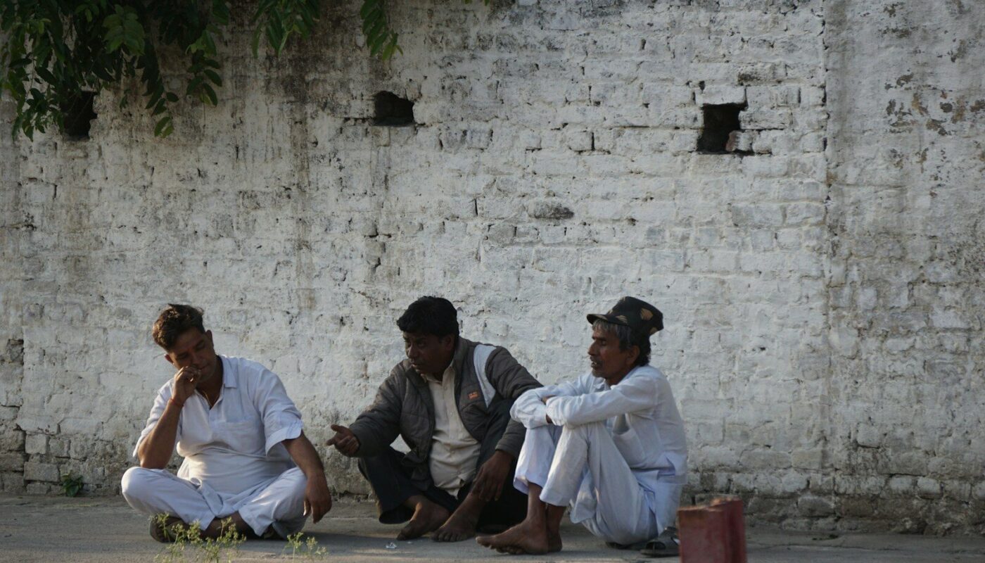 three people sitting on the ground near a brick wall