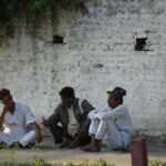 three people sitting on the ground near a brick wall