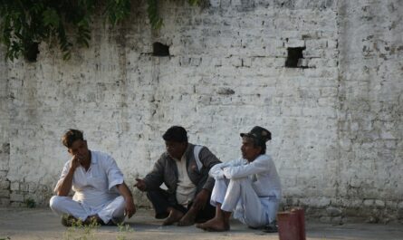 three people sitting on the ground near a brick wall