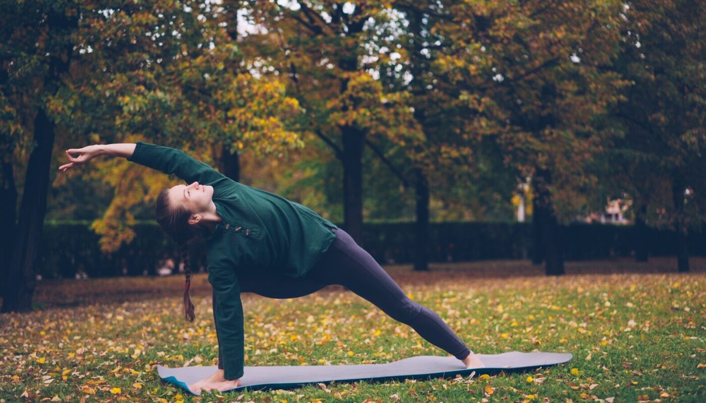 Woman practicing yoga on mat in autumn park