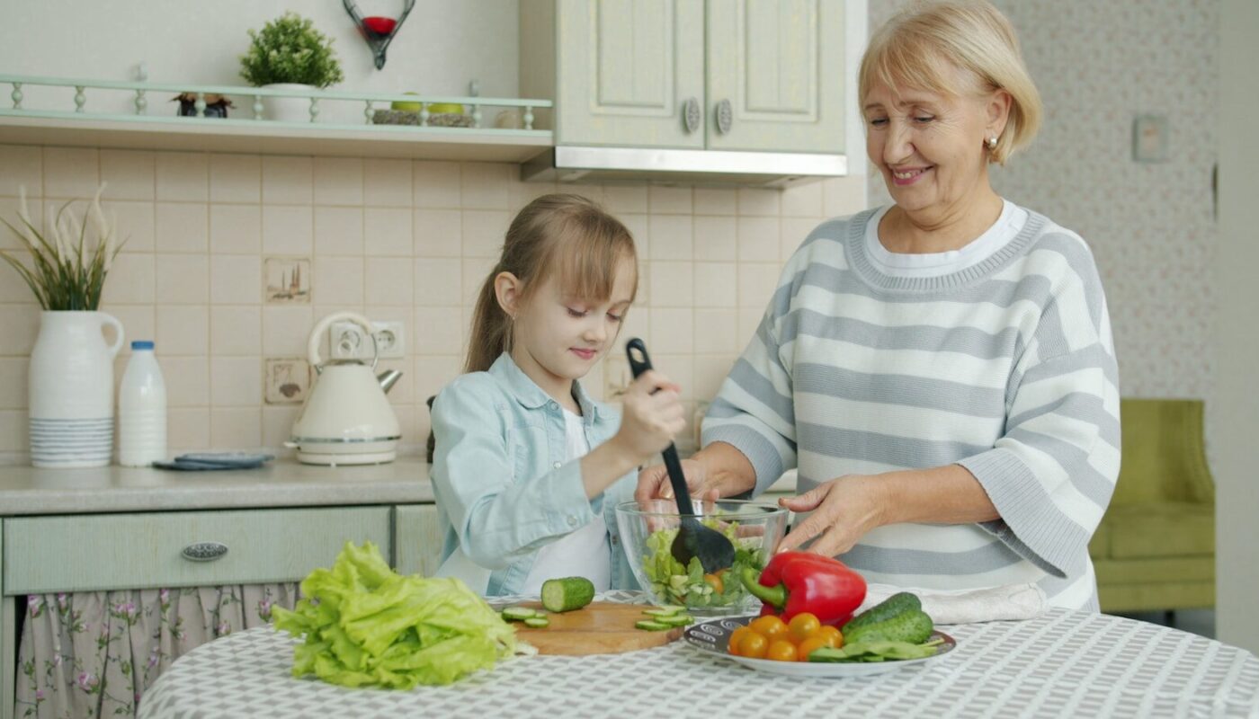 Grandmother and granddaughter making salad together in kitchen.