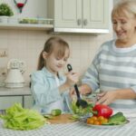 Grandmother and granddaughter making salad together in kitchen.